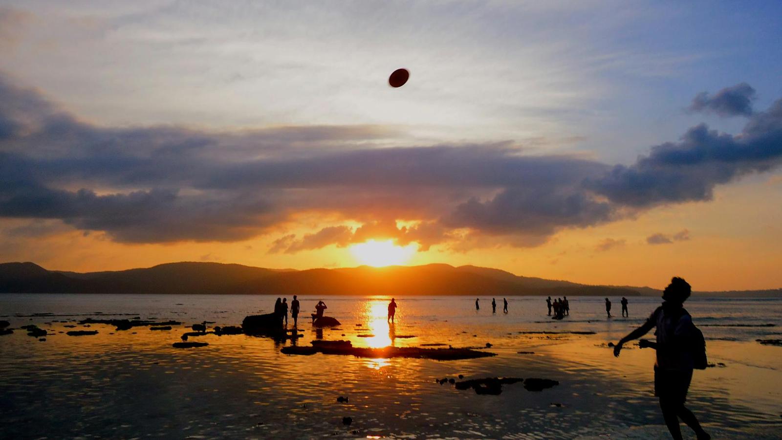 Silhouetted beachgoers playing at low tide against a glowing orange sunset