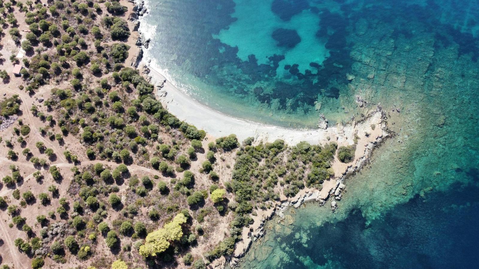 An aerial view of a rocky cove with turquoise water and green scrub