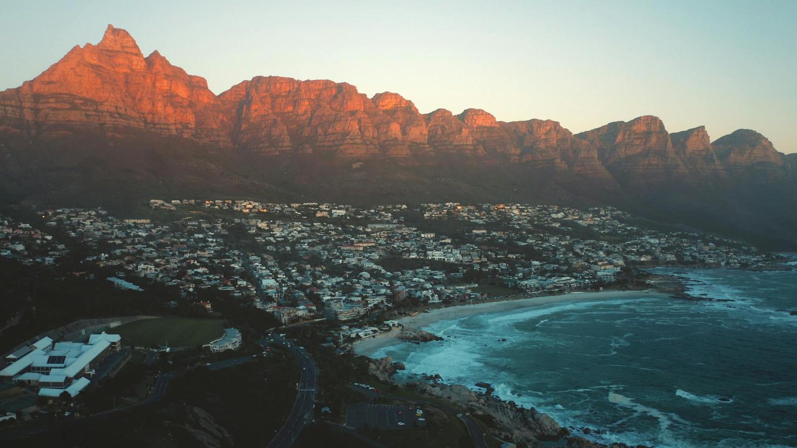 Jagged mountains glow red at sunset above a coastal town and beach