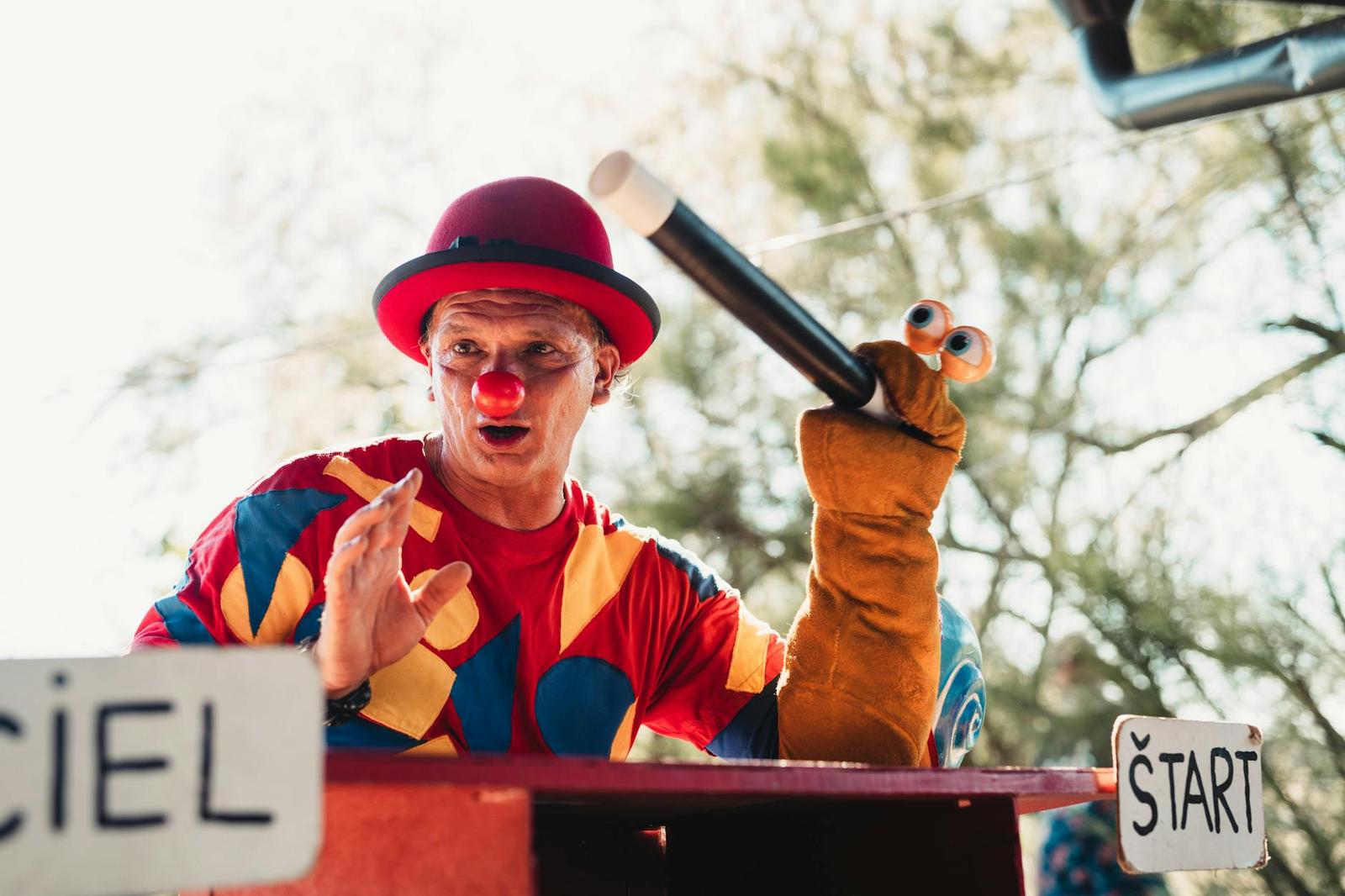 A clown performer in a red bowler hat holding a hand puppet on stage
