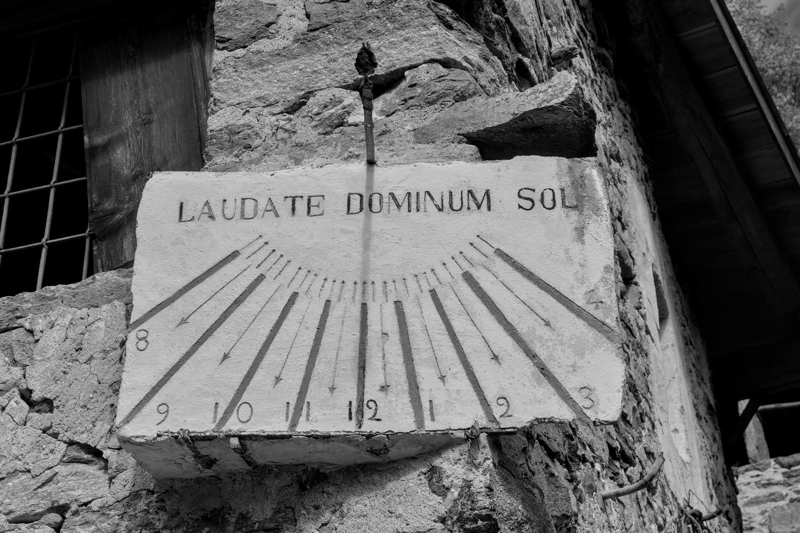 Black and white photo of a stone sundial with a Latin inscription on a weathered wall