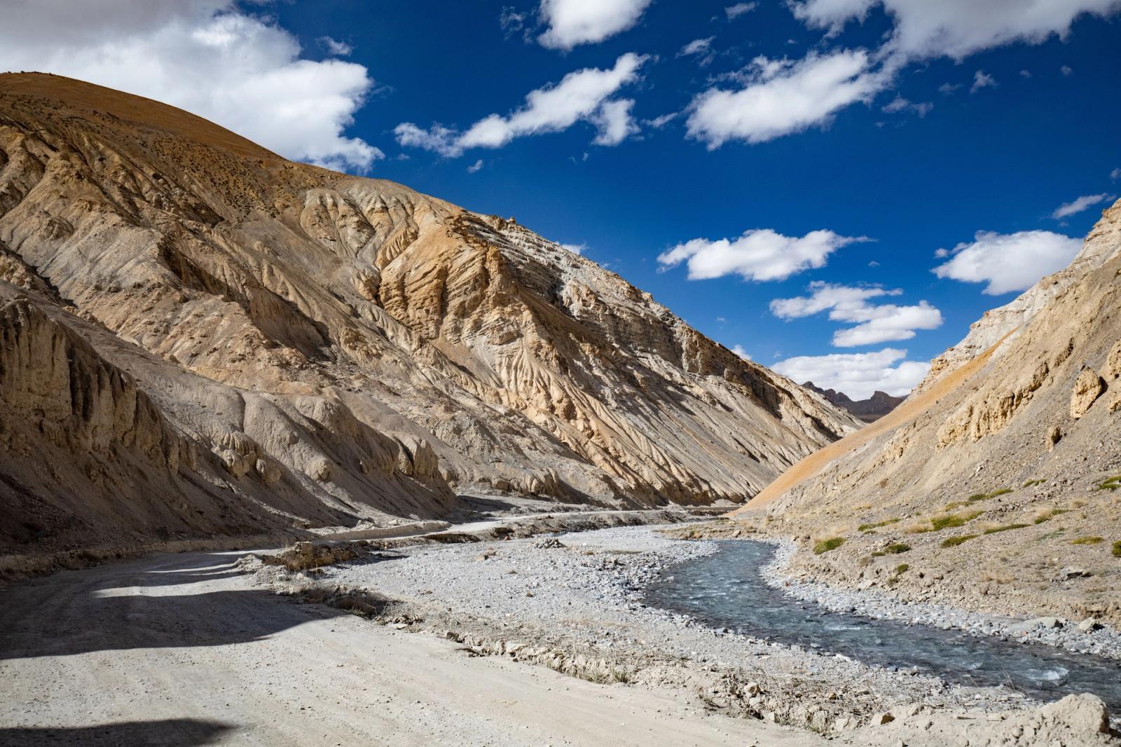 A dry riverbed winding through a layered mountain gorge