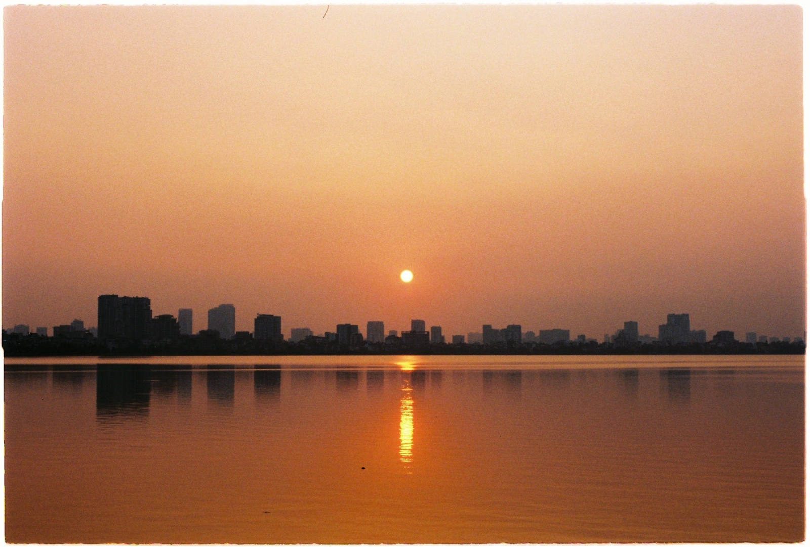 Serene sunset over Hanoi's West Lake, with city skyline reflections and warm hues lighting the sky