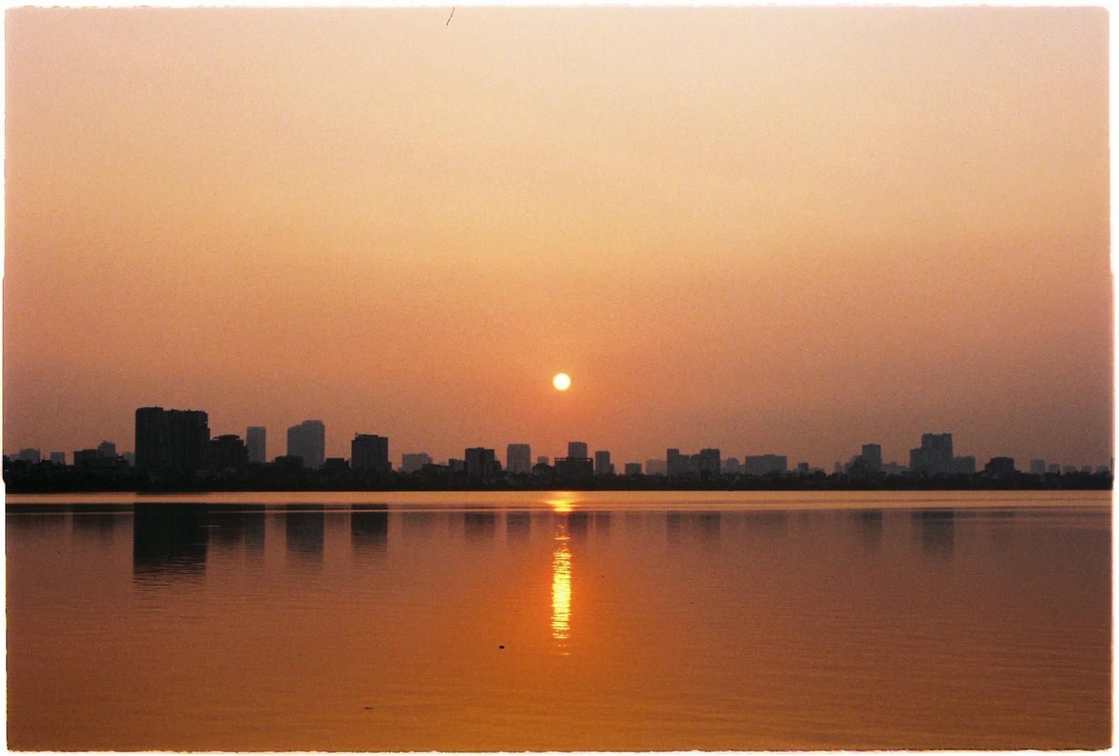 Serene sunset over Hanoi's West Lake, with city skyline reflections and warm hues lighting the sky