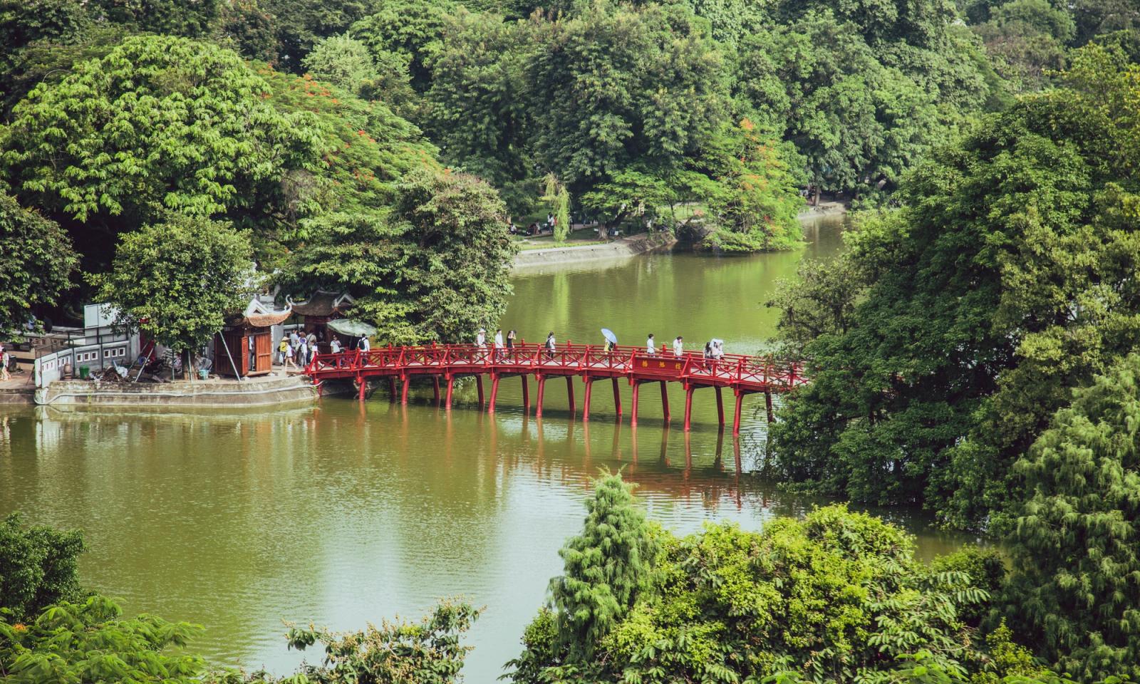 A scenic red bridge spans a calm river in a lush, green forest setting, inviting exploration