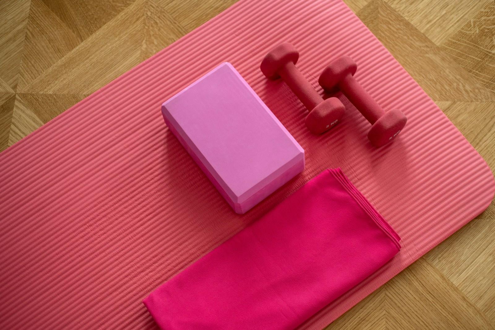A yoga mat laid out with dumbbells, a block and a towel