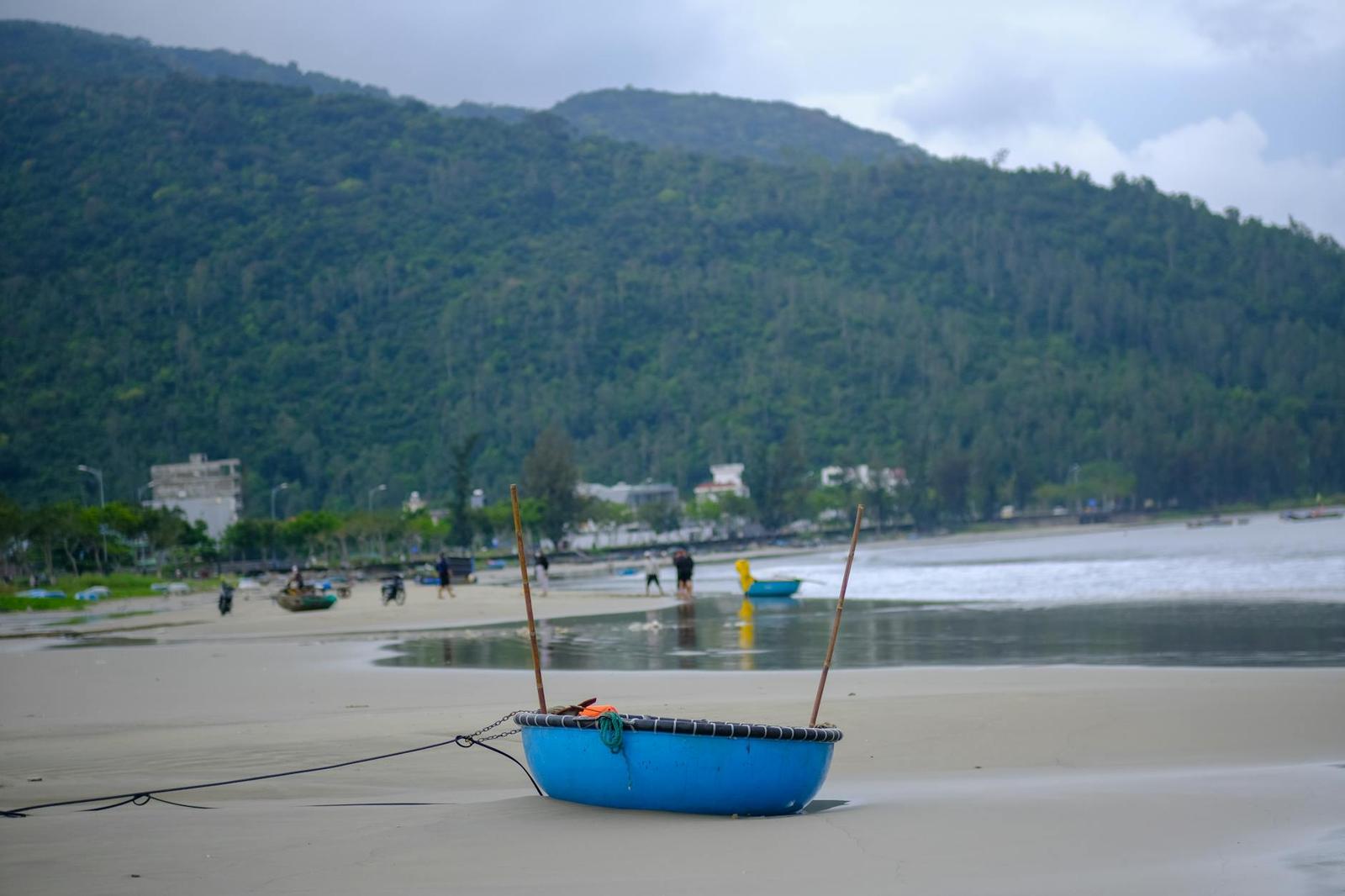 A small blue boat resting on a beach with distant figures near the shoreline