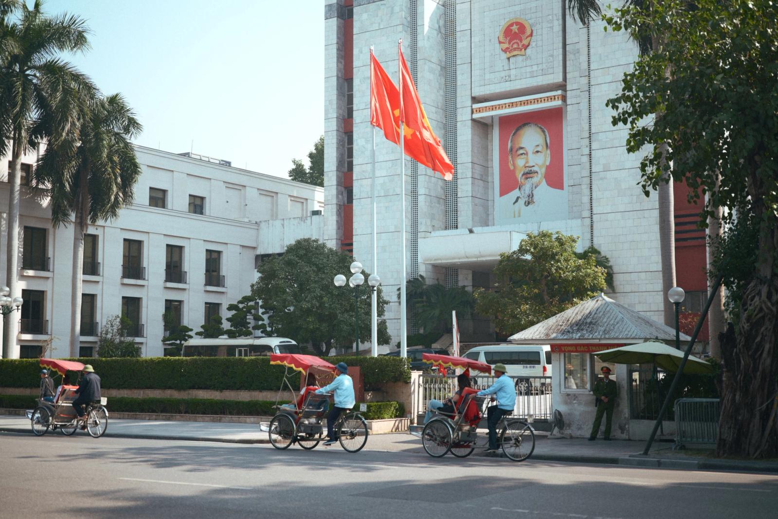 Cyclo riders passing by government building in Hanoi, Vietnam