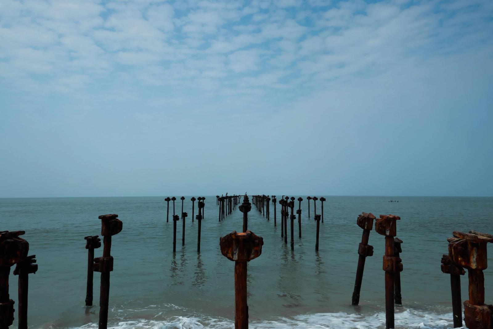 View of rusty pier remains stretching into the calm Arabian Sea under a blue sky in Alappuzha, Kerala, India