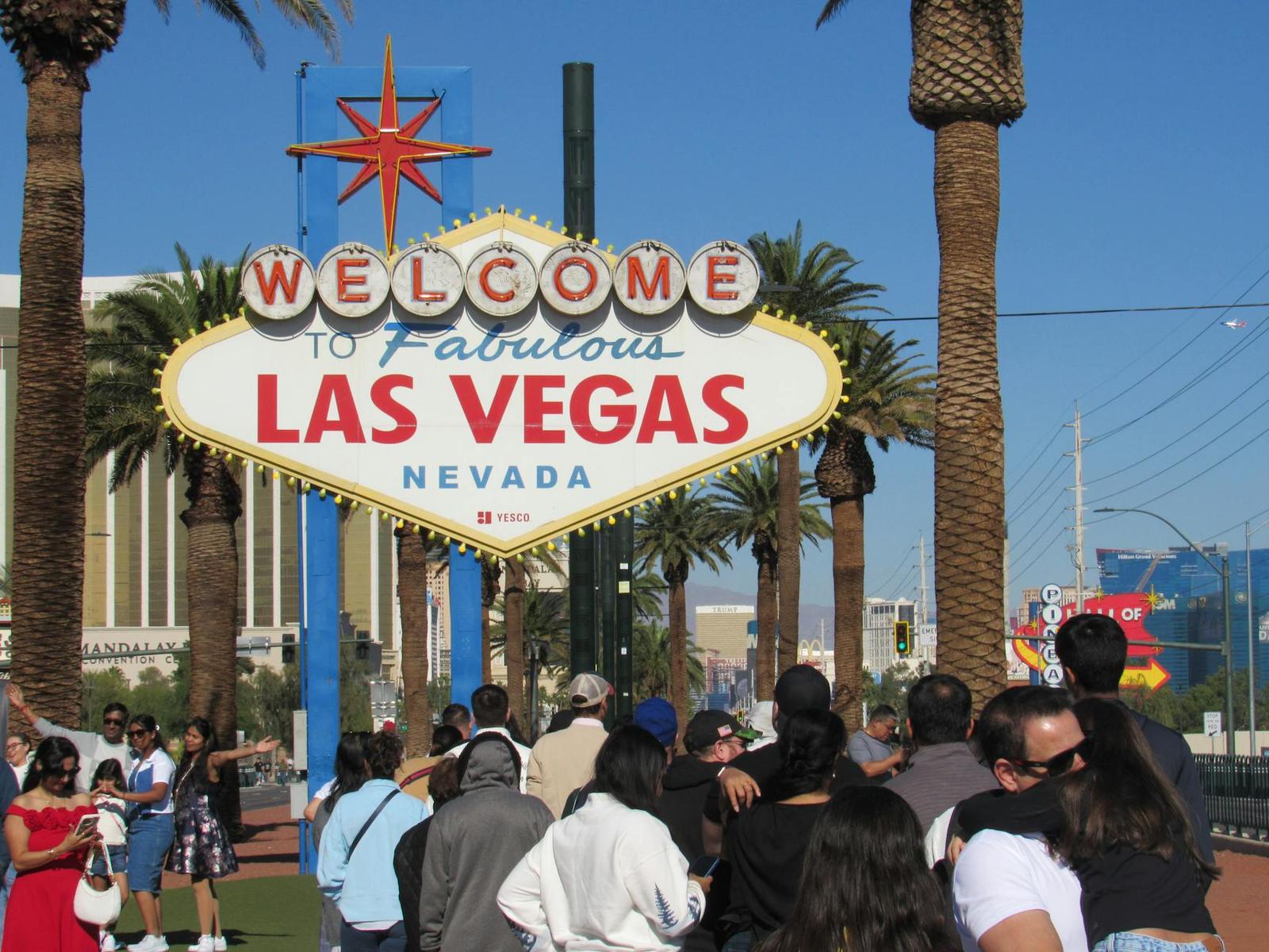 A crowd of visitors gathered beneath a welcome to Las Vegas sign among palm trees