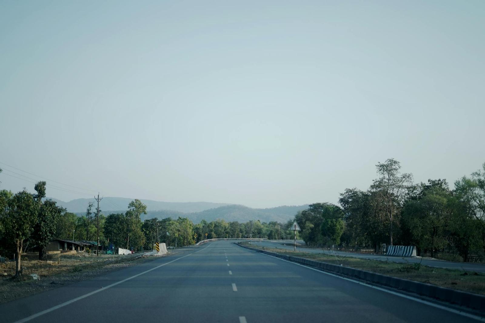 An empty two-lane highway lined with trees stretching toward hills