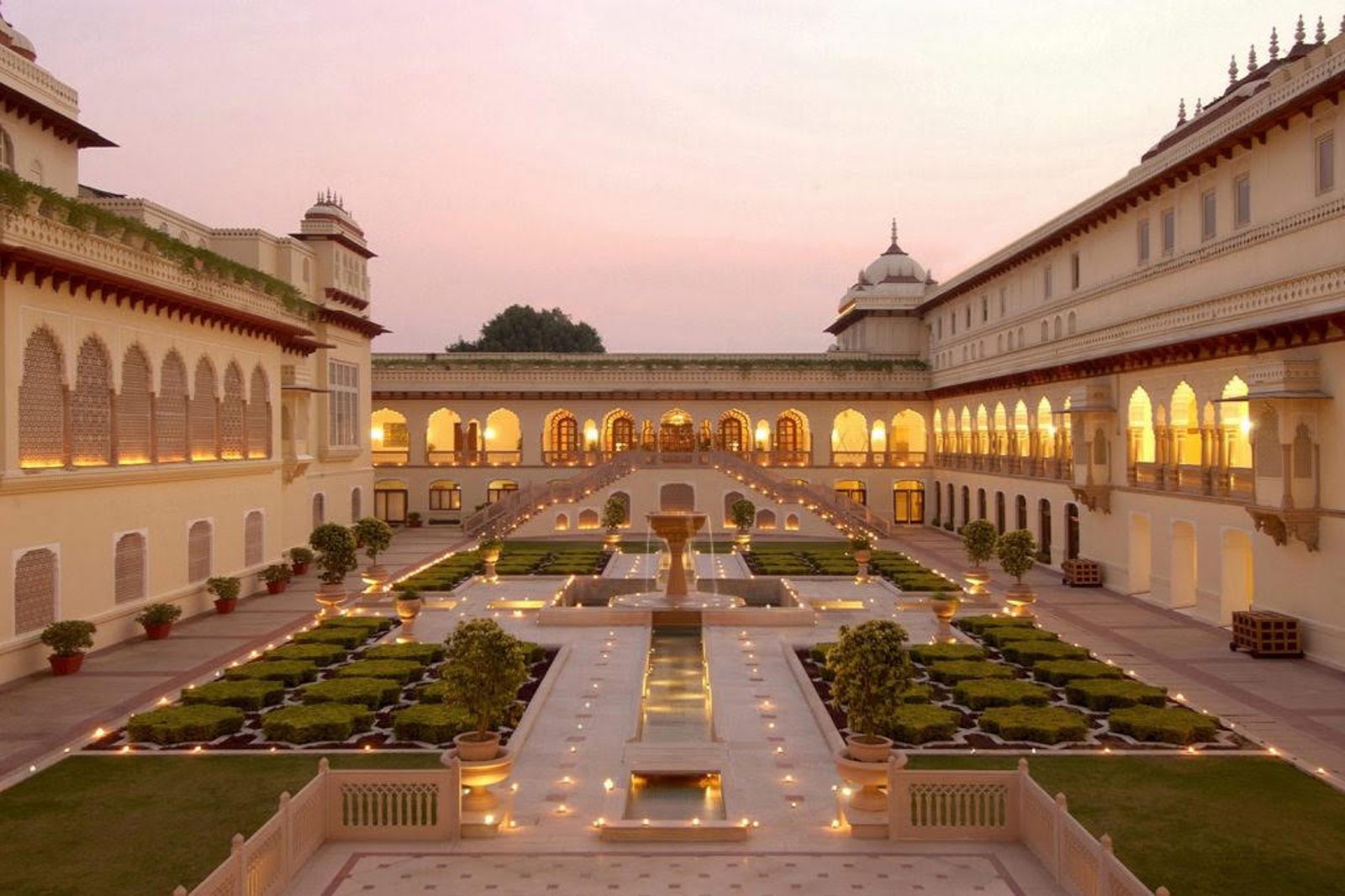 Courtyard of Rambagh Palace in Jaipur at dusk, reflecting pool lined with lights