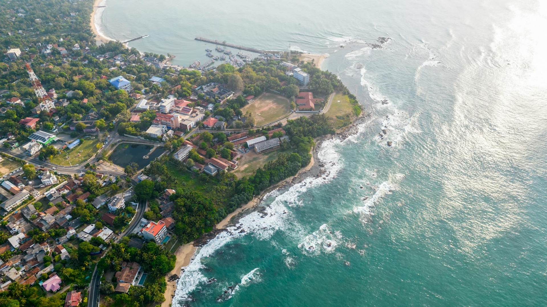 Aerial view of a coastal town where green headland meets turquoise surf