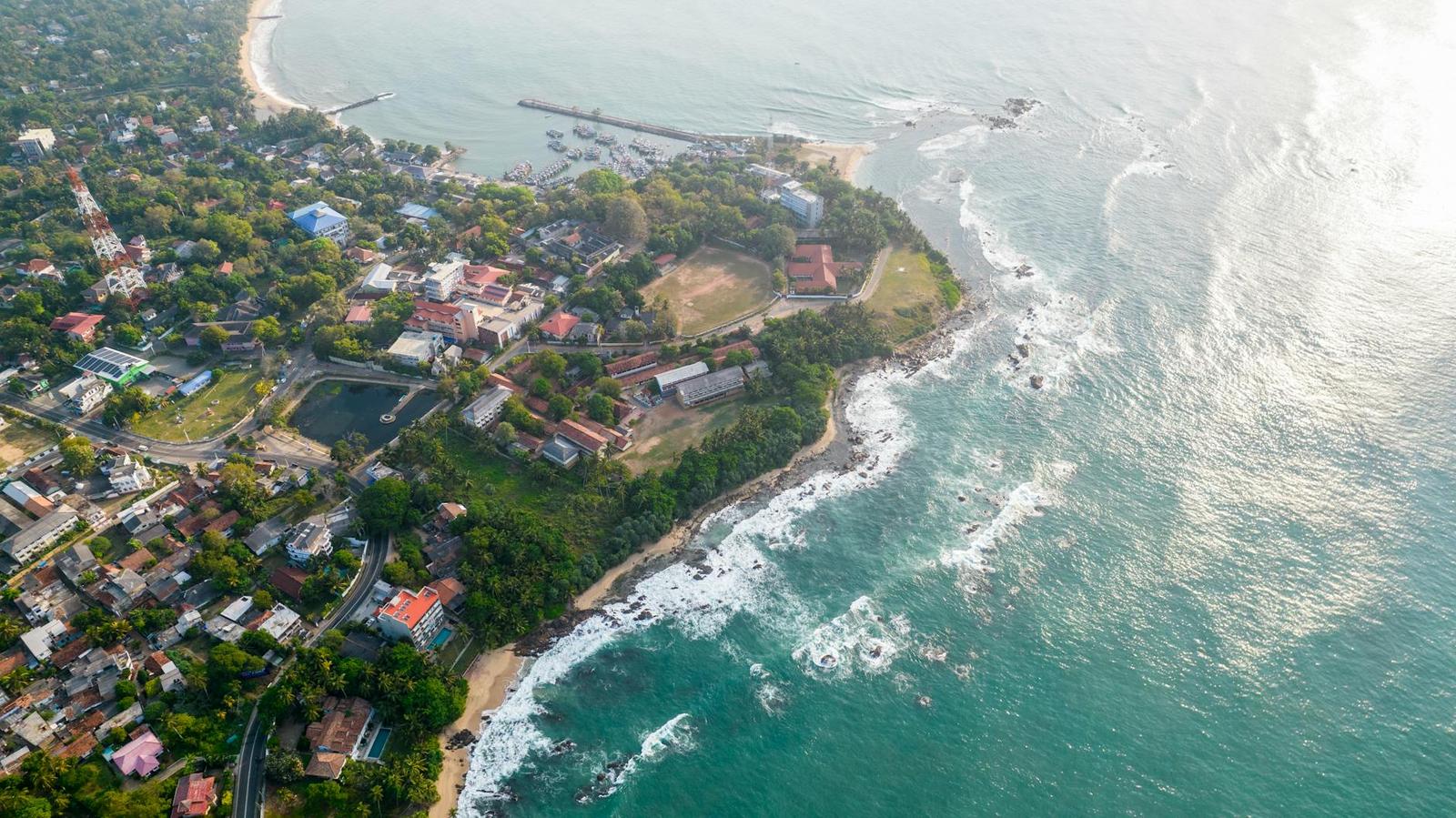 Aerial view of a coastal town where green headland meets turquoise surf