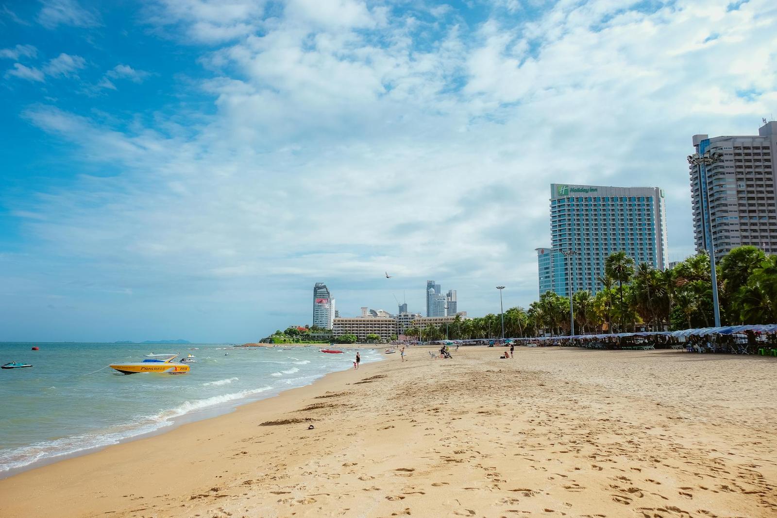 A sandy beach along a bay with high-rise towers and palm trees in the distance
