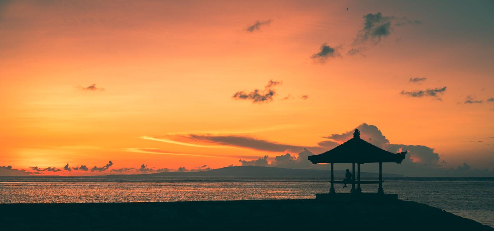A silhouetted beachside pavilion against a fiery orange sunset