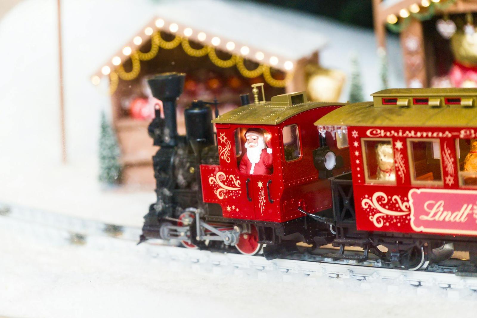 A miniature toy train with a Santa figure passing a lit holiday display