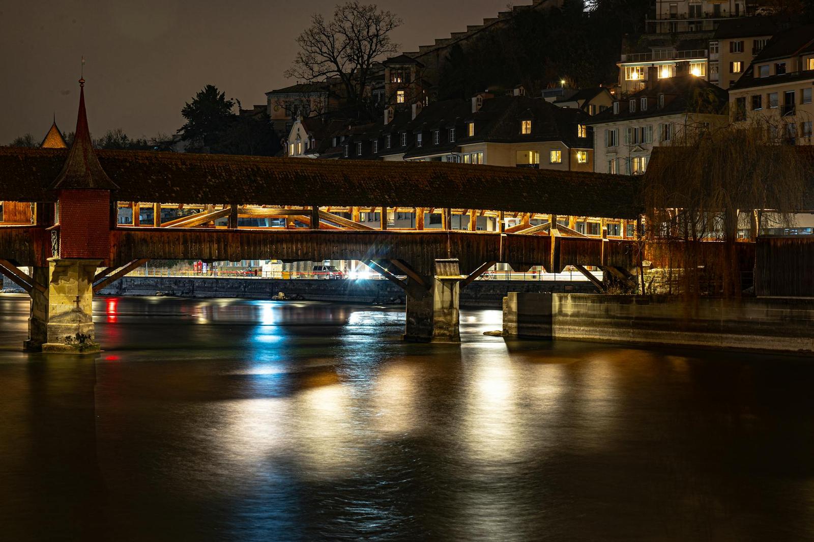 A covered wooden bridge lit at night reflecting on a calm river