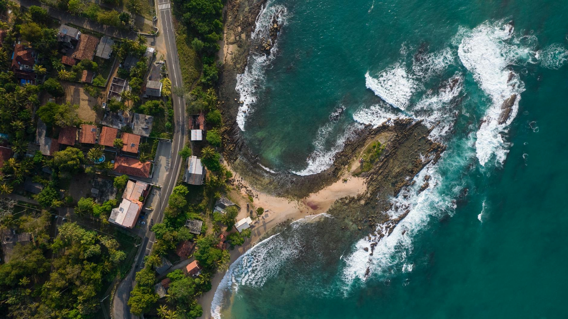 Aerial view of a rocky cove with a small beach beside a coastal road