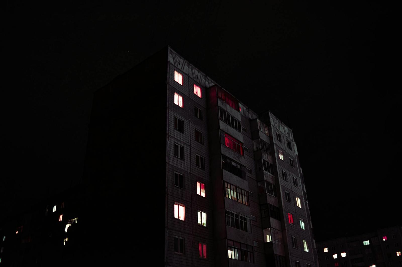 A dark high-rise apartment block at night with scattered lit windows glowing red and white