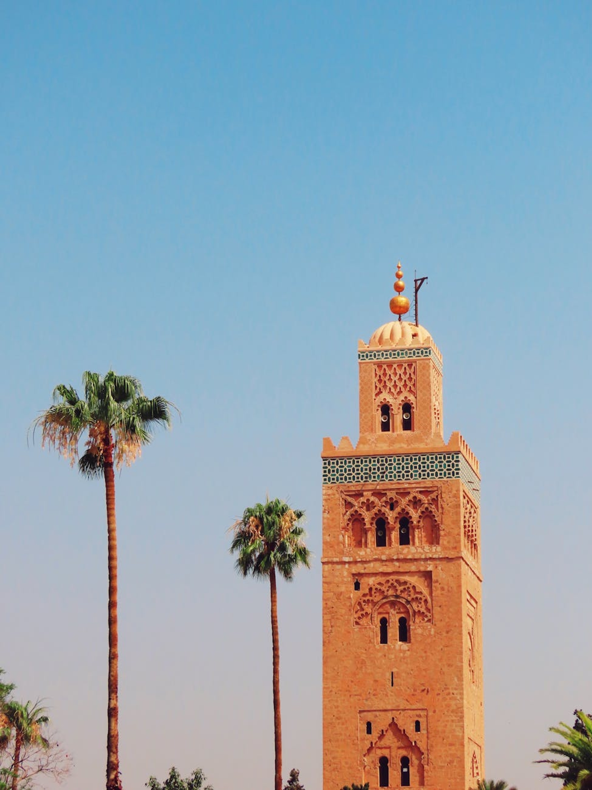 Iconic Koutoubia Mosque tower with palm trees in Marrakech against a clear blue sky