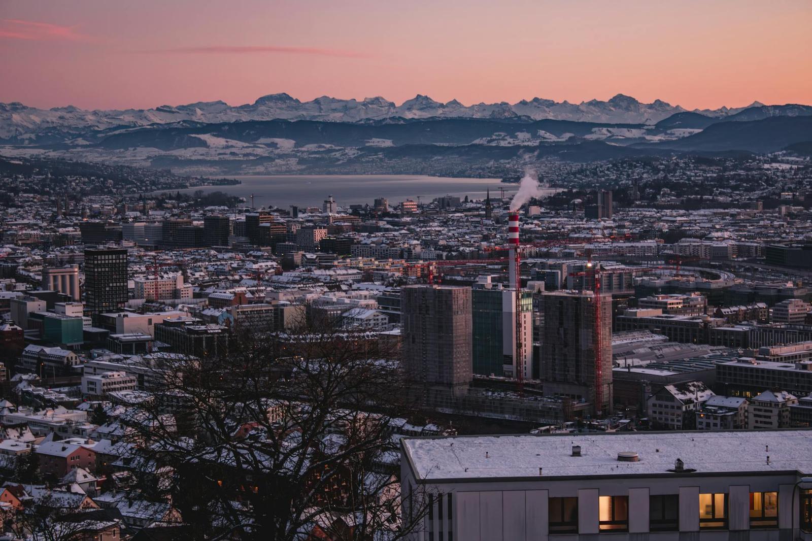 City skyline at dusk with snow-capped mountains on the horizon