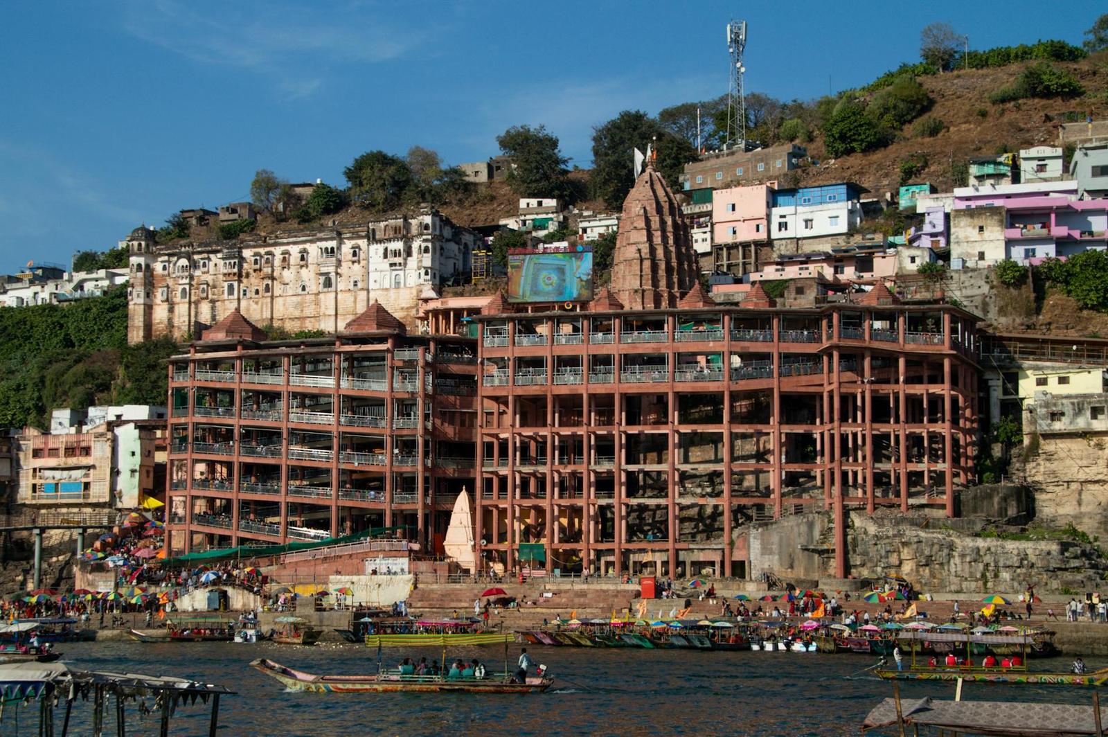 A riverside temple complex with tiered balconies and boats moored below