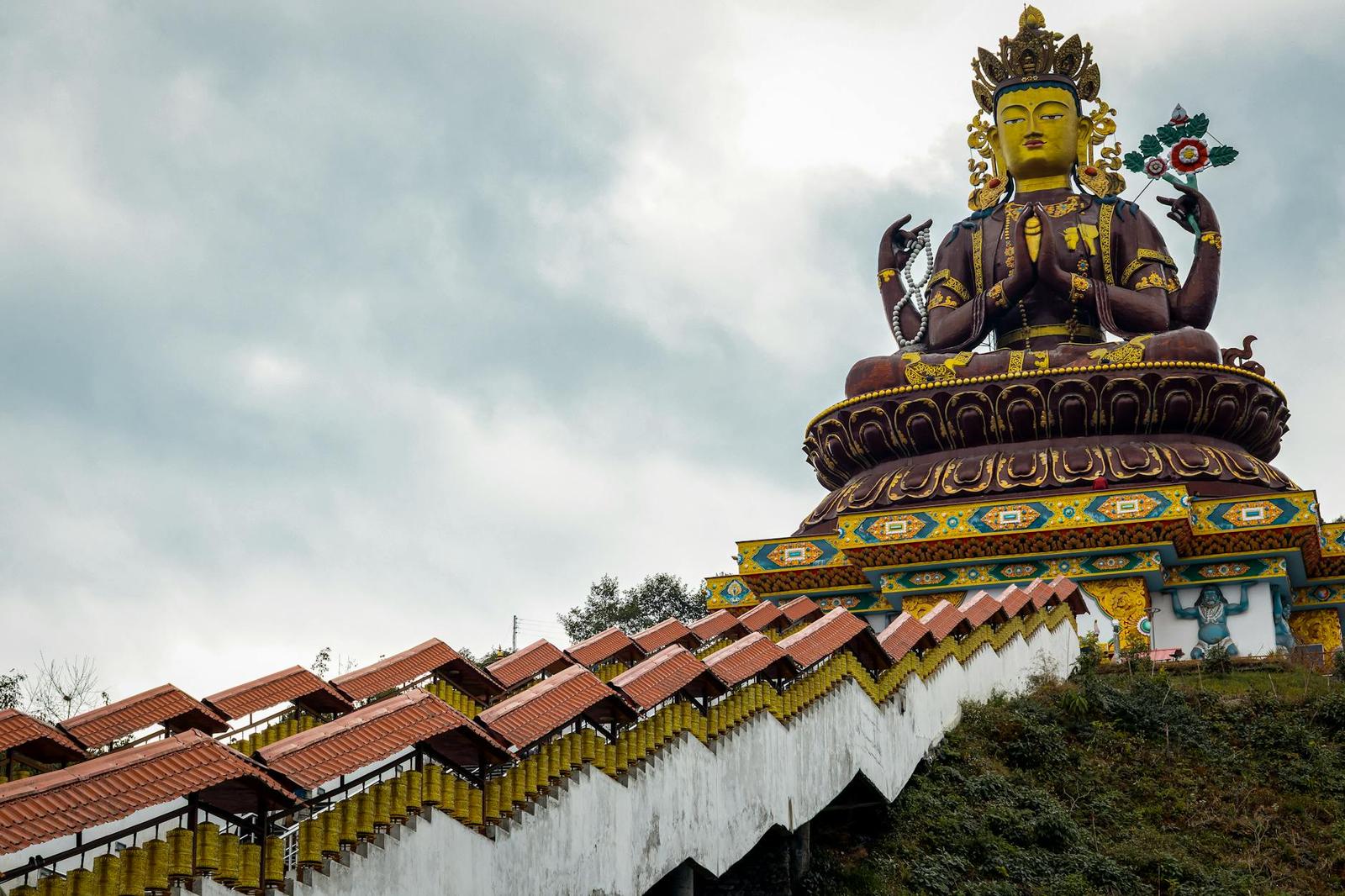 A golden multi armed deity statue atop a hillside temple complex