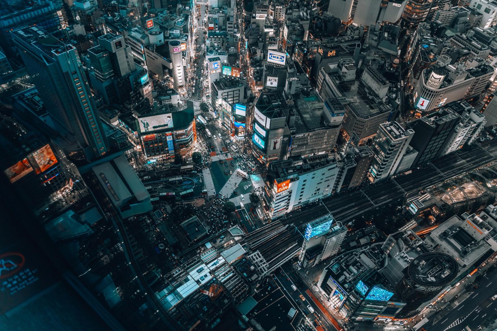 A dynamic aerial shot of Shibuya Crossing in Tokyo at night, showcasing vibrant city lights