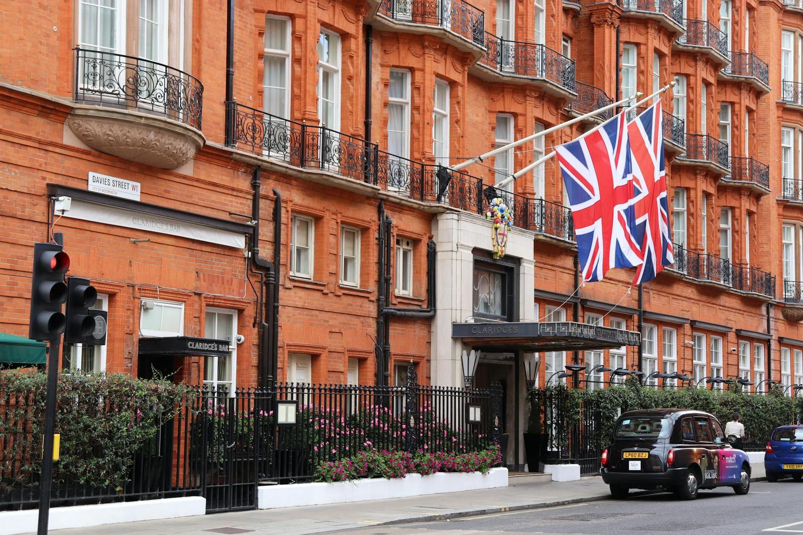 A red brick hotel facade with union jack flags and a black cab parked outside