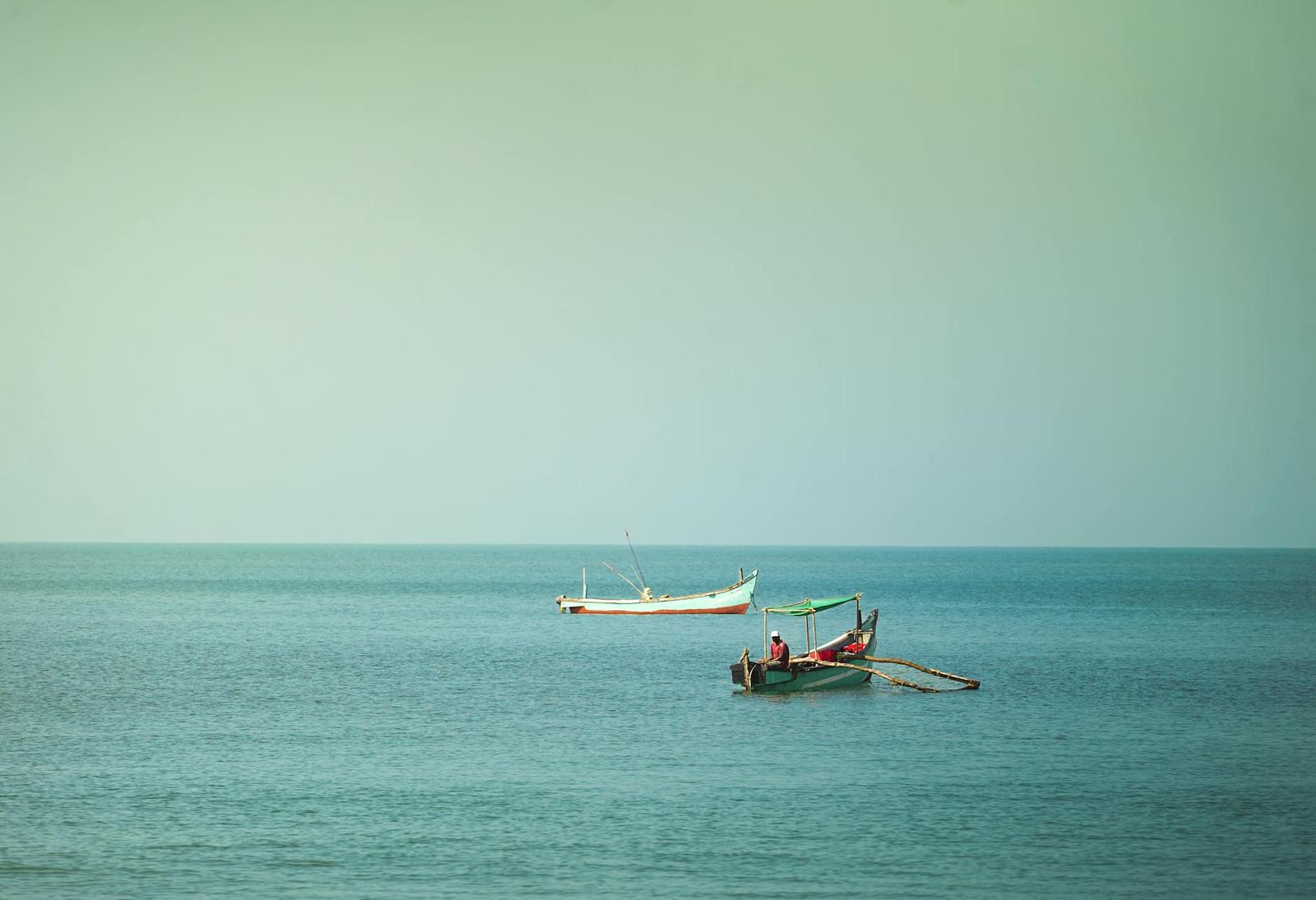 Two small fishing boats drifting on a calm sea under a pale sky