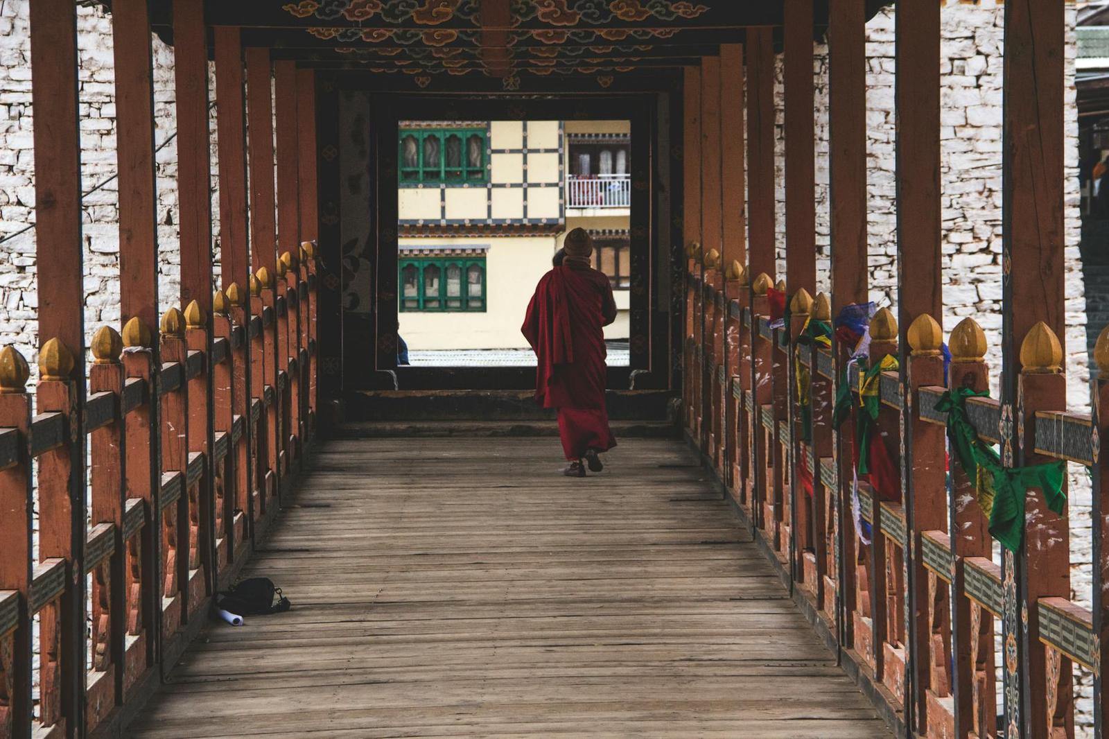 A robed monk walking through a long covered bridge corridor