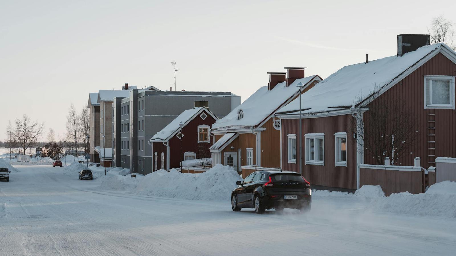 Car driving down a snow-cleared residential street lined with timber houses