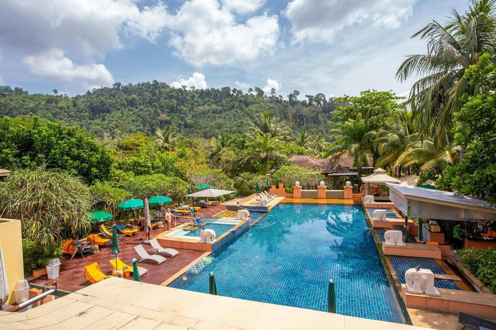An aerial view of a resort pool surrounded by loungers and tropical hillside greenery