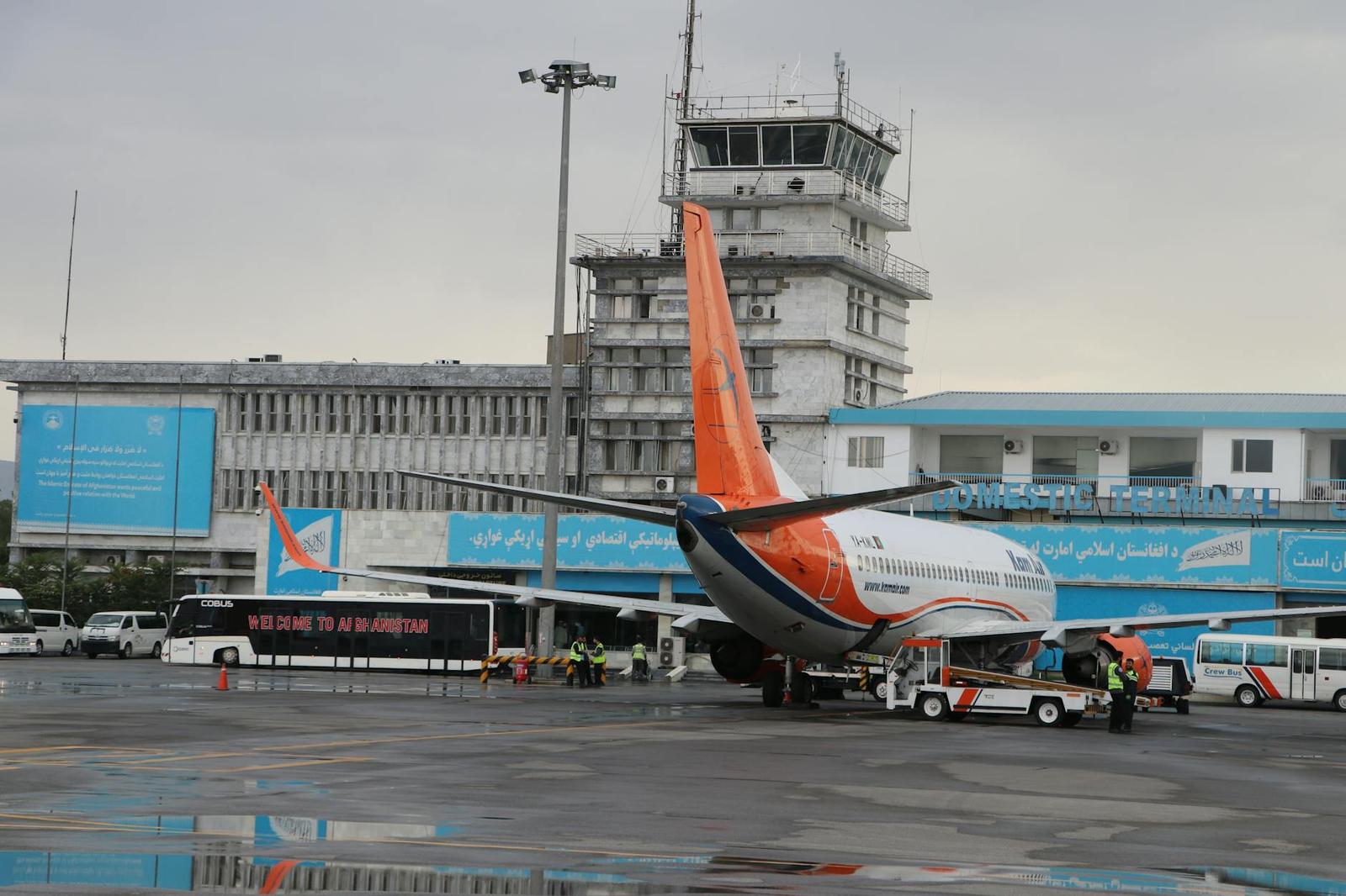 An airplane parked on a rain-soaked tarmac beside a control tower