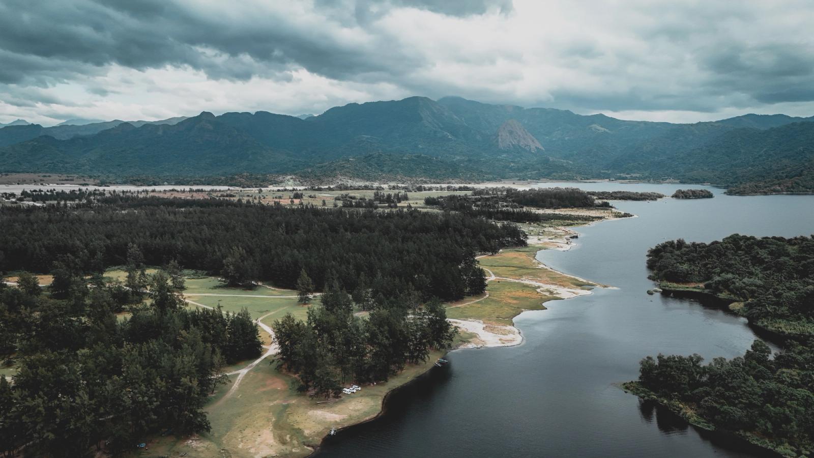 Stunning aerial shot of a river winding through lush forest with majestic mountains in the background