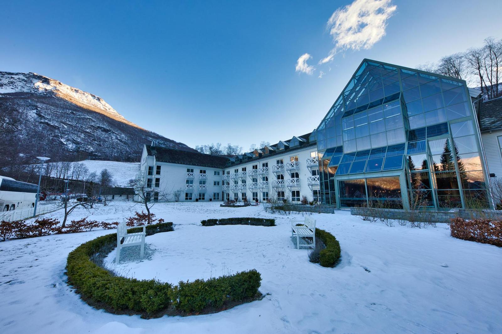 A glass-fronted hotel building overlooking a snowy courtyard below mountains