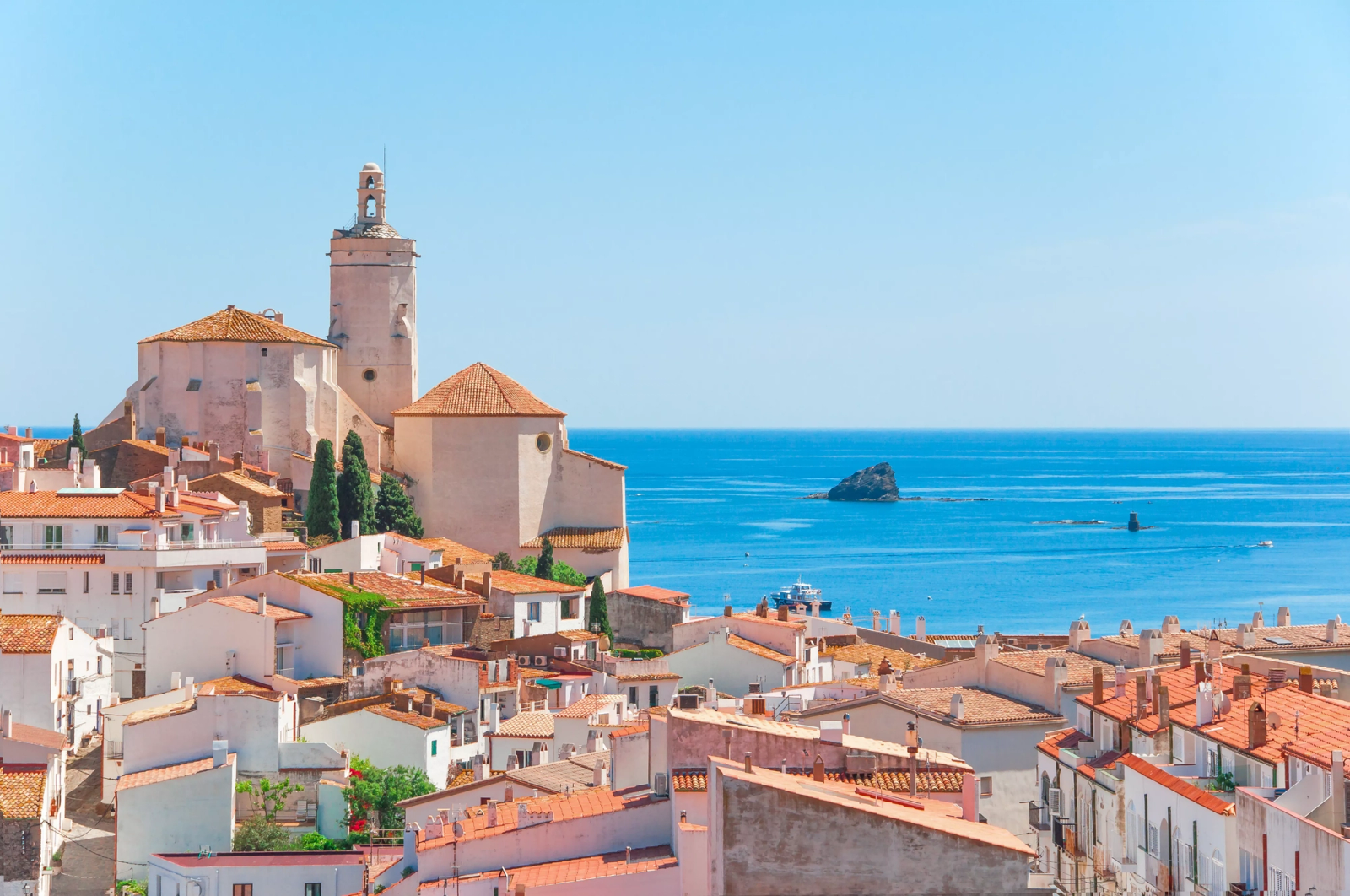 A coastal town of red-roofed houses clusters below a church tower beside the sea