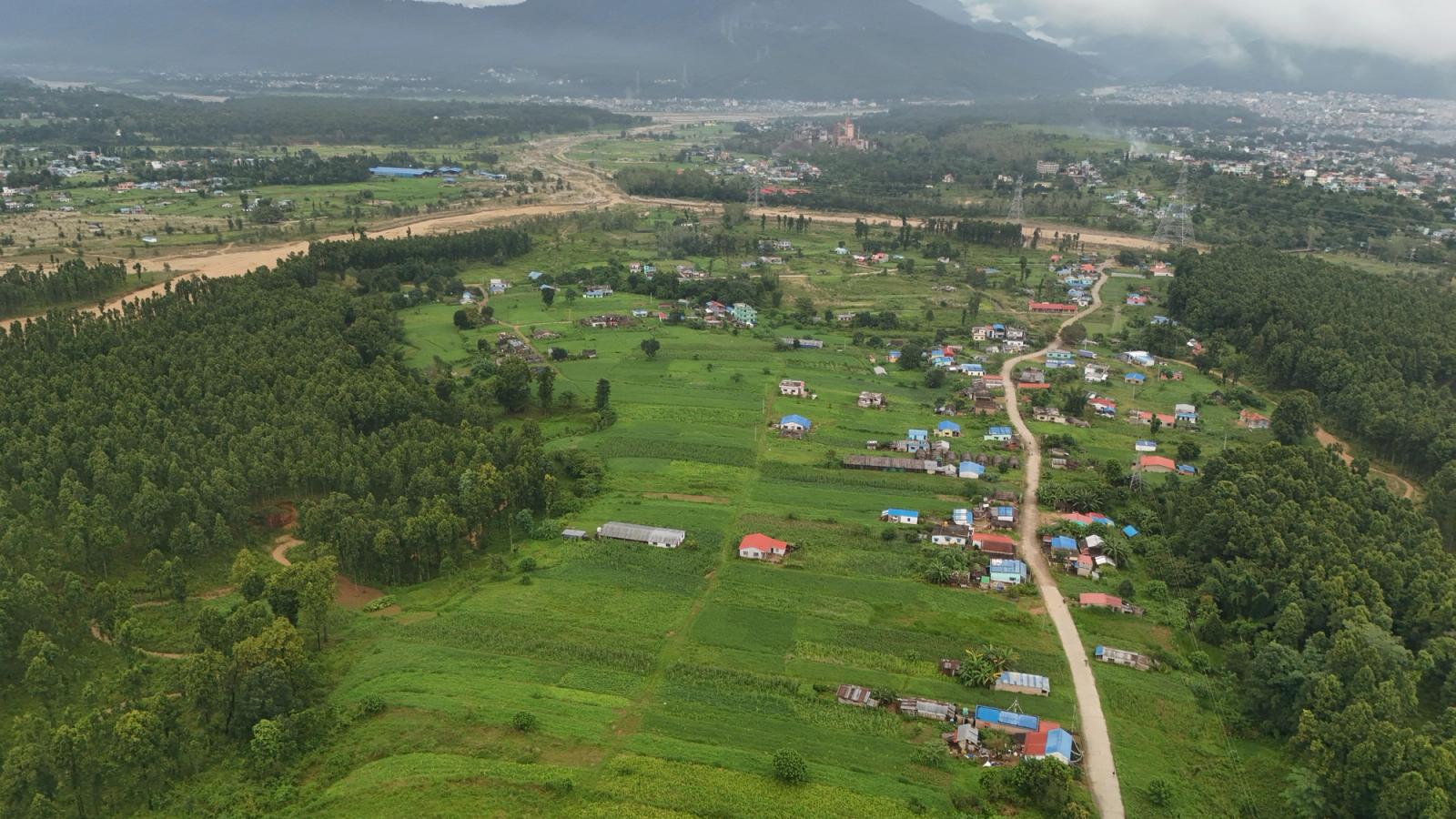 A stunning aerial view showcasing lush green fields and a small village in Nepal, surrounded by trees and hills