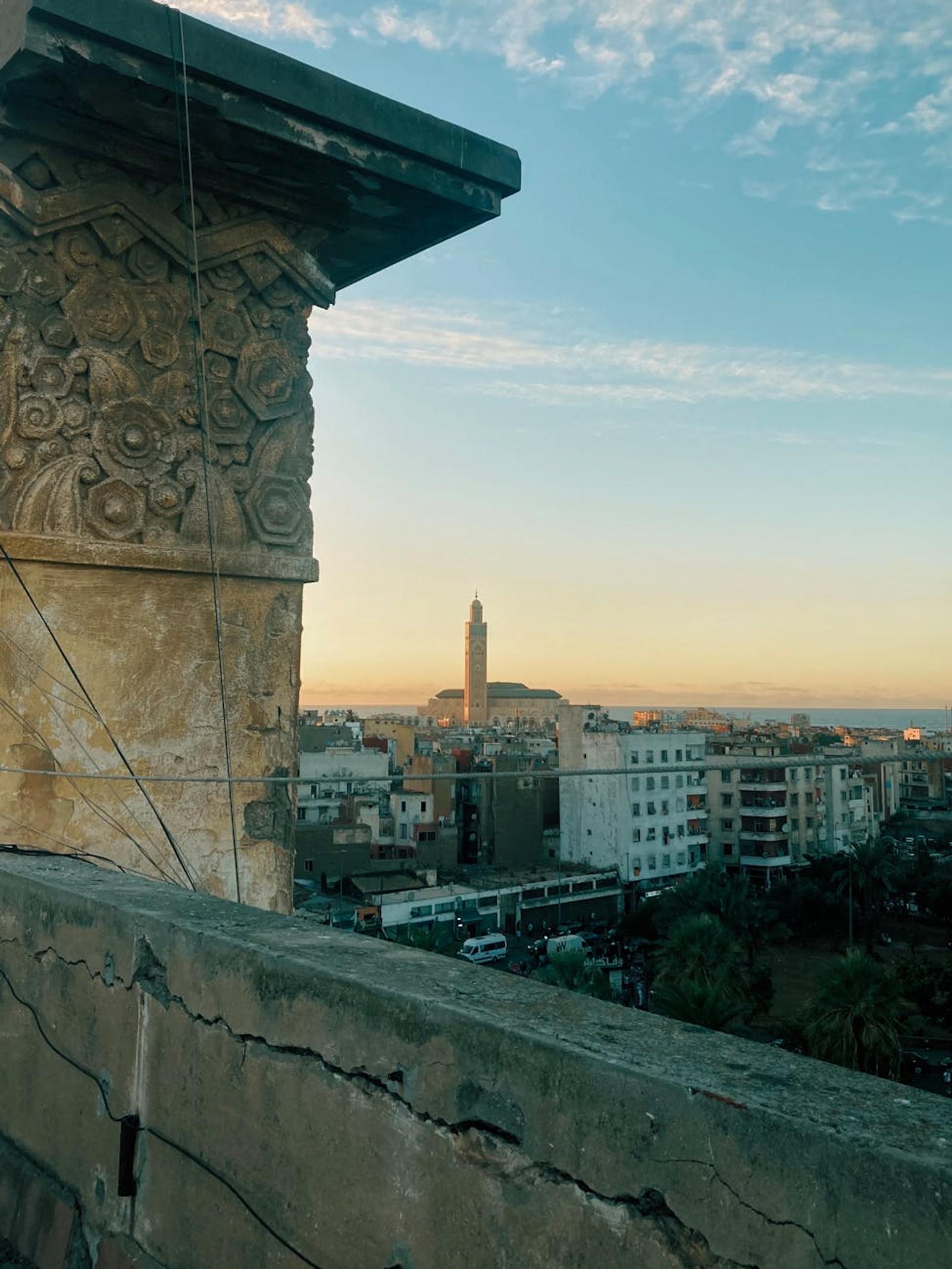 Carved stone column framing a distant minaret and coastal city at sunset