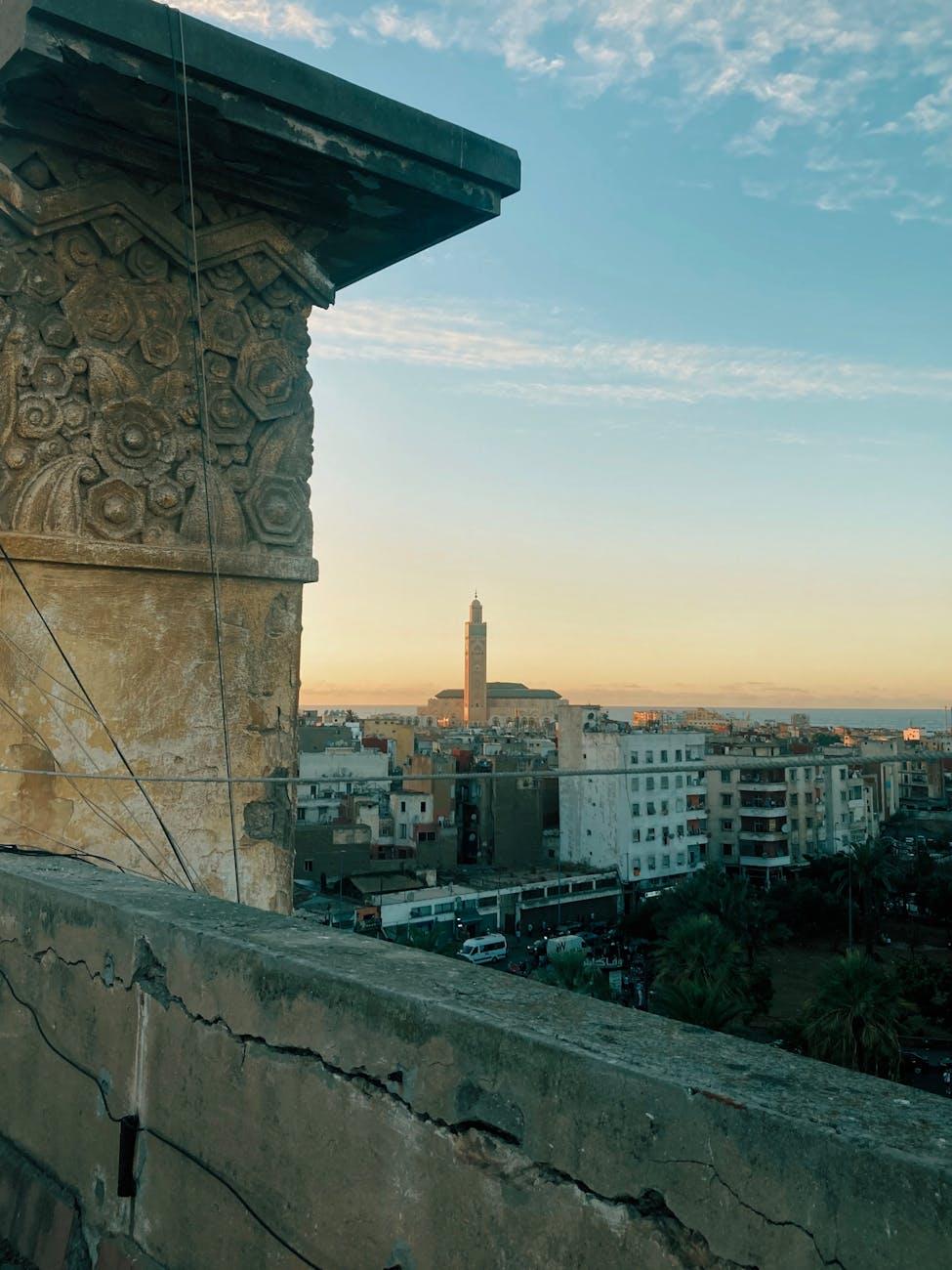Carved stone column framing a distant minaret and coastal city at sunset