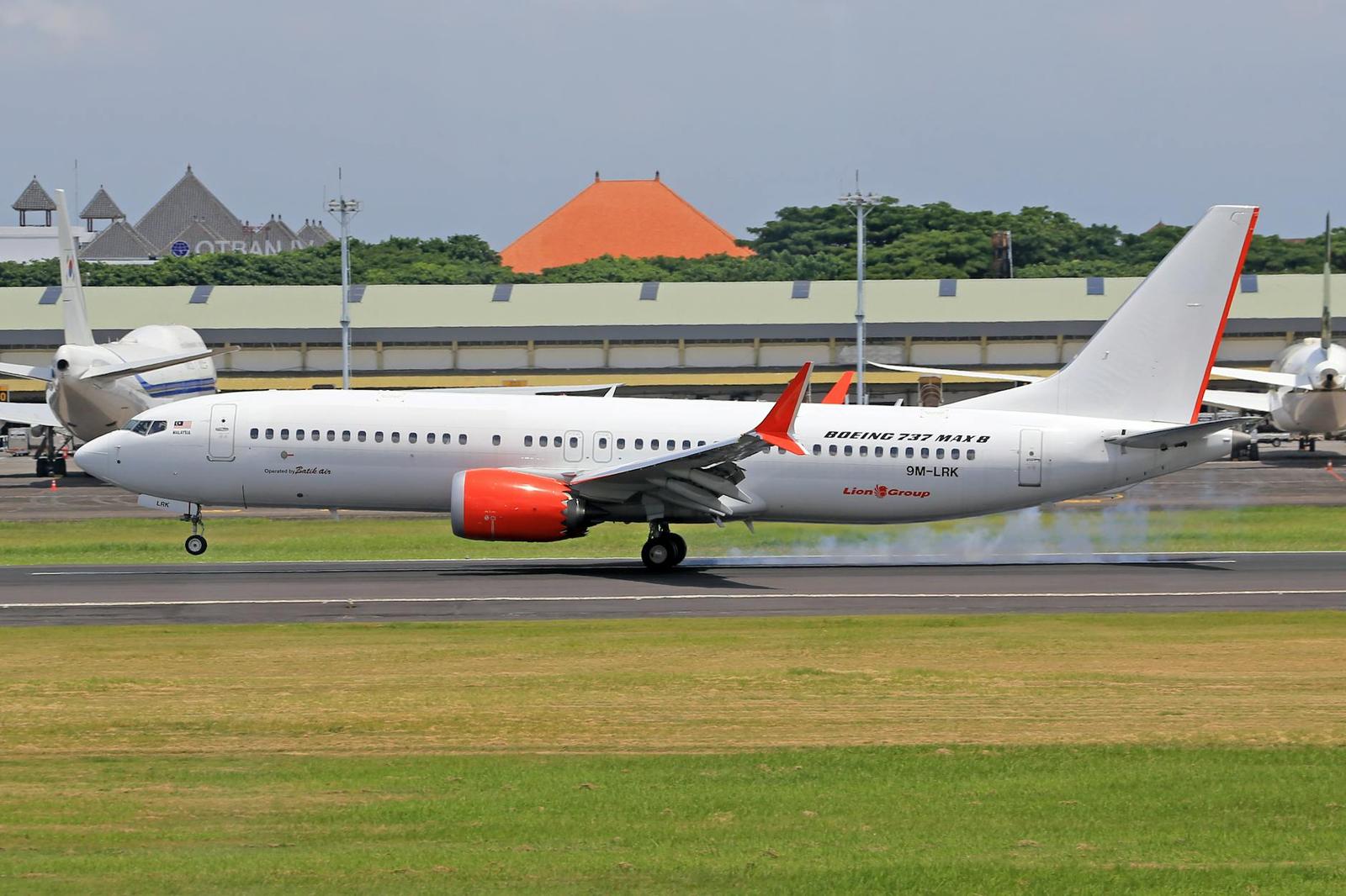 A passenger jet taxiing on the runway past a tiled pavilion roof