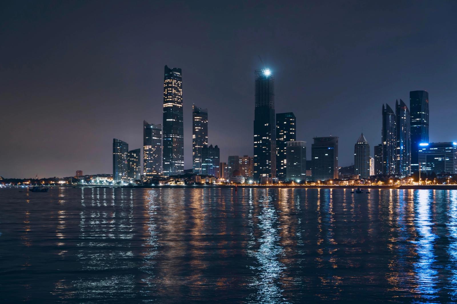 Night view of Abu Dhabi skyline with reflections on water, showcasing modern architecture
