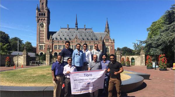 A group of men posing with a banner in front of a historic building.