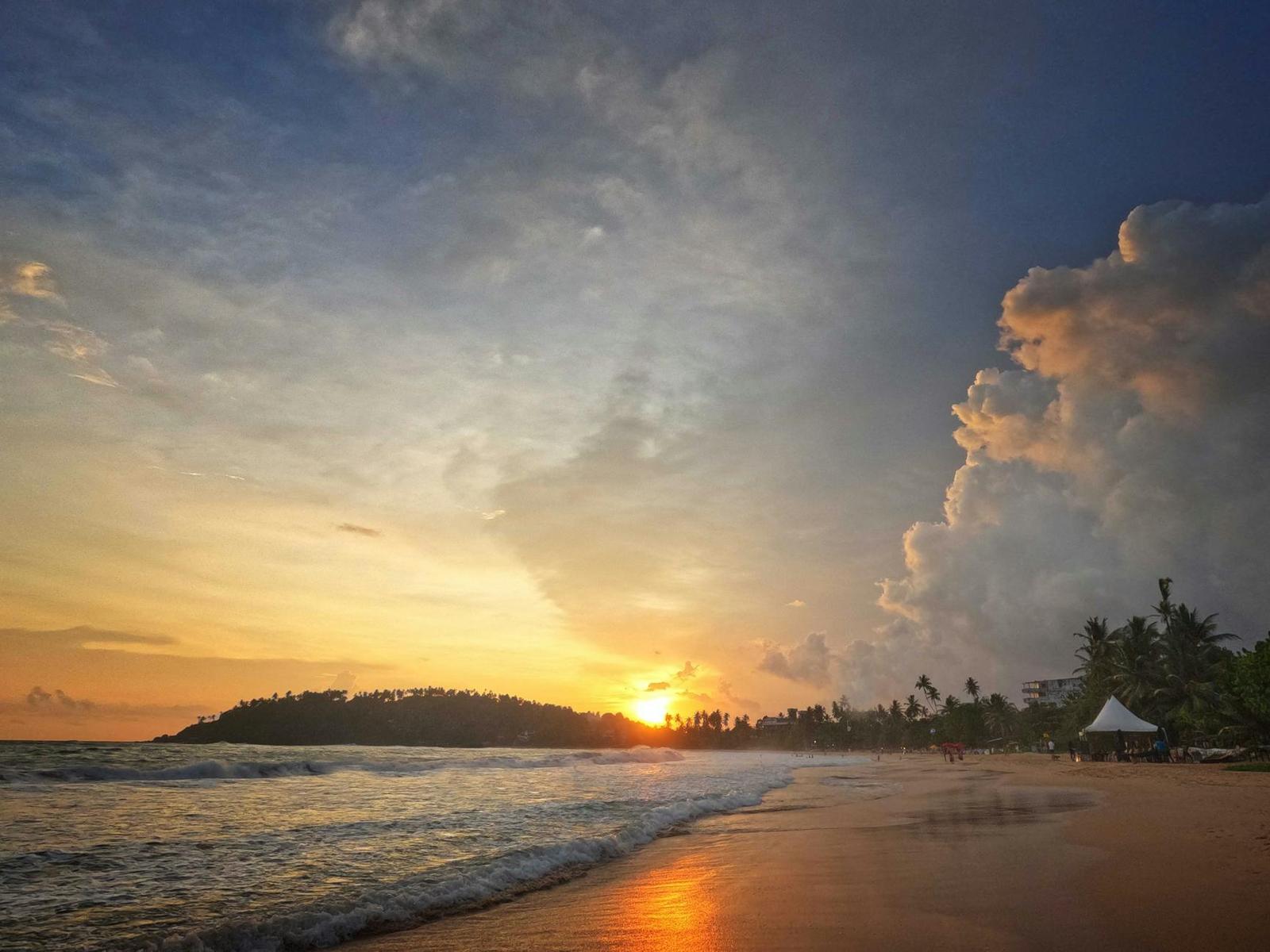 Sun setting over a palm-fringed beach with towering storm clouds