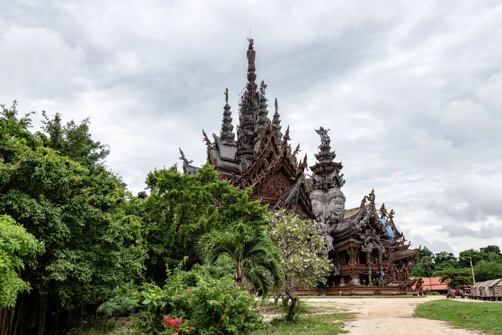 The Sanctuary of Truth in Pattaya, Thailand, showcasing intricate wooden carvings against a verdant backdrop