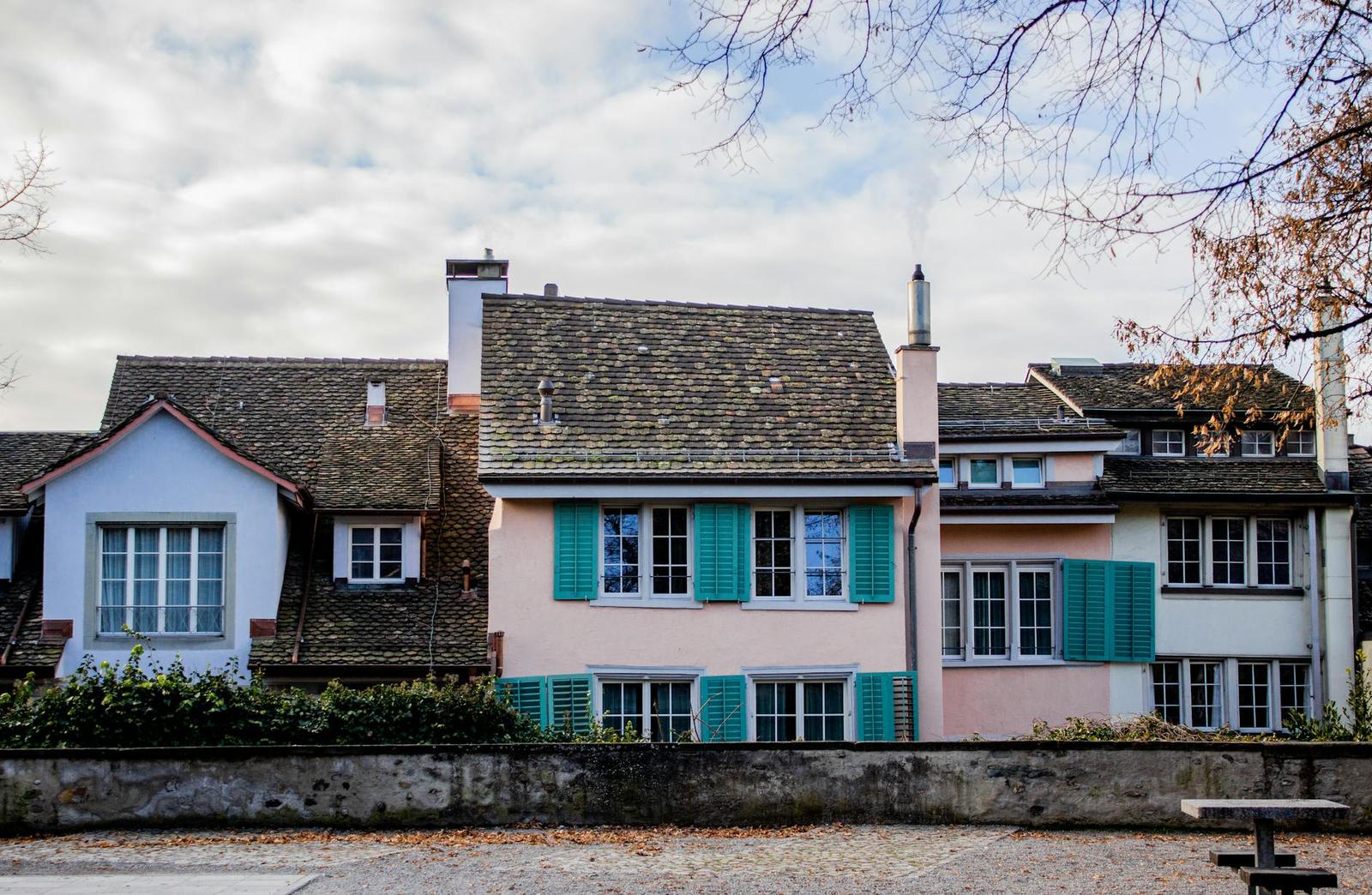 Row of pastel gabled houses with teal shutters along a quiet street