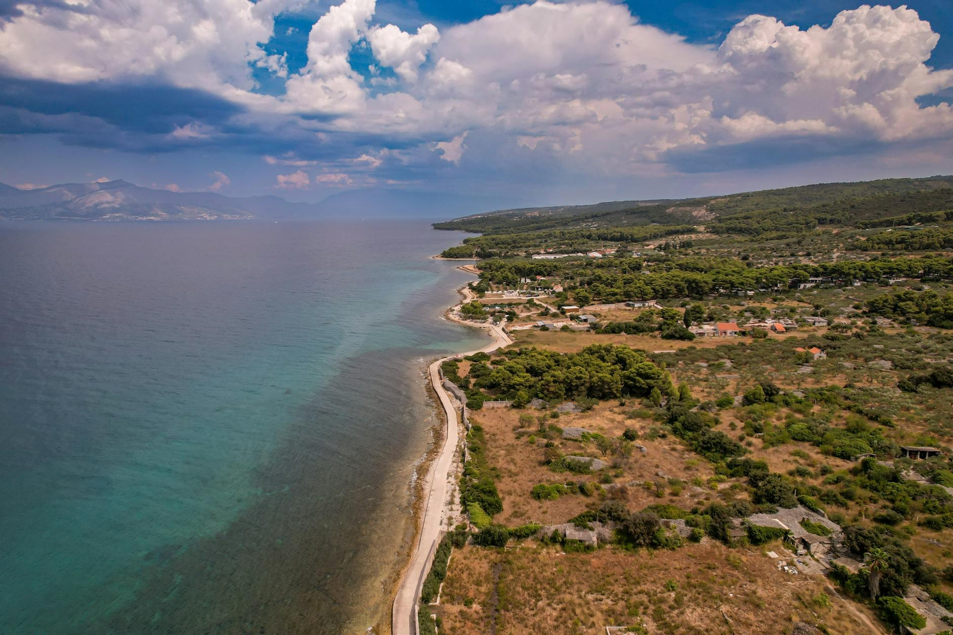 Aerial view of a rocky coastline meeting turquoise water under clouds