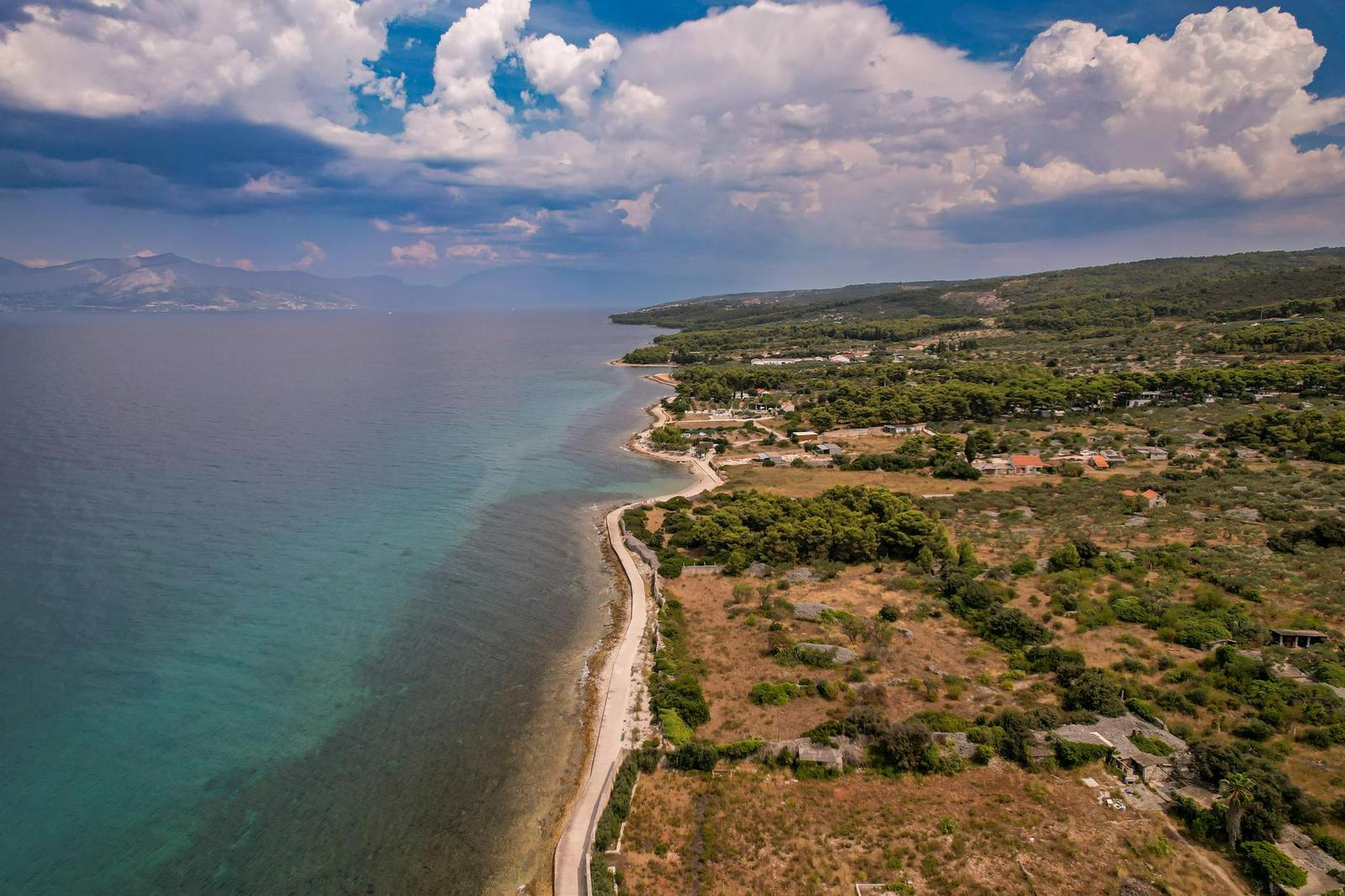 Aerial view of a rocky coastline meeting turquoise water under clouds