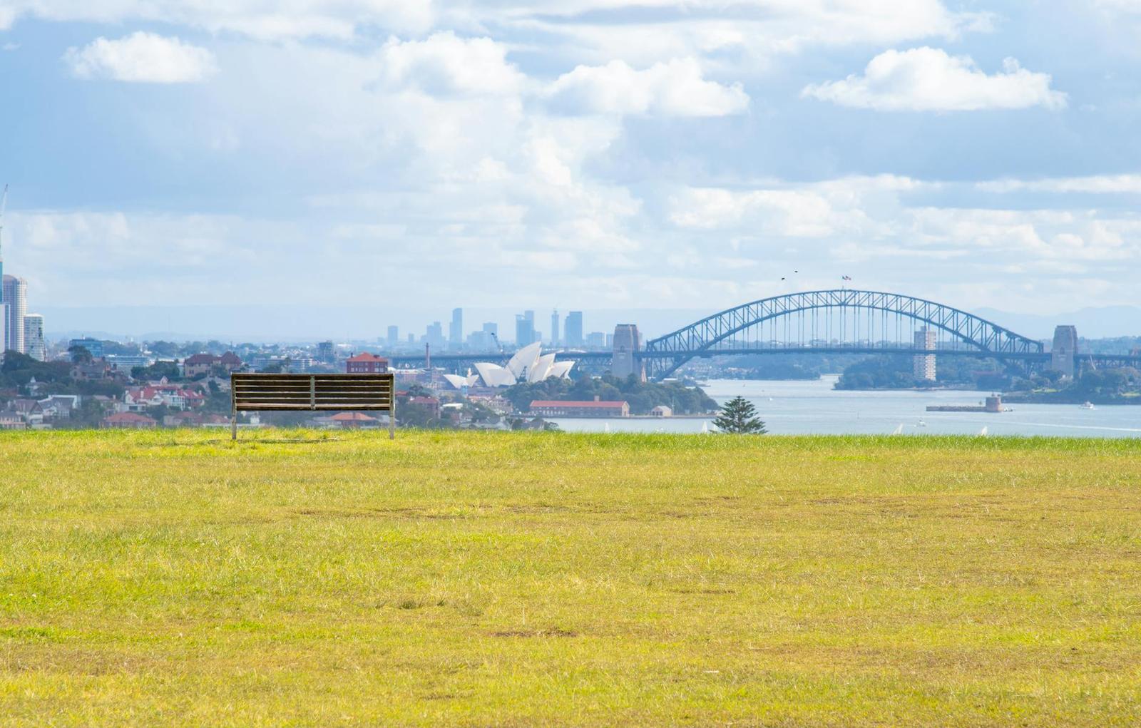 A park bench overlooking a harbour bridge and opera house across the water